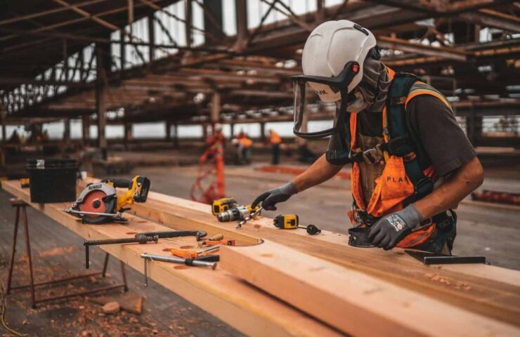Man met helm die houten planken zaagt met zaagmachine